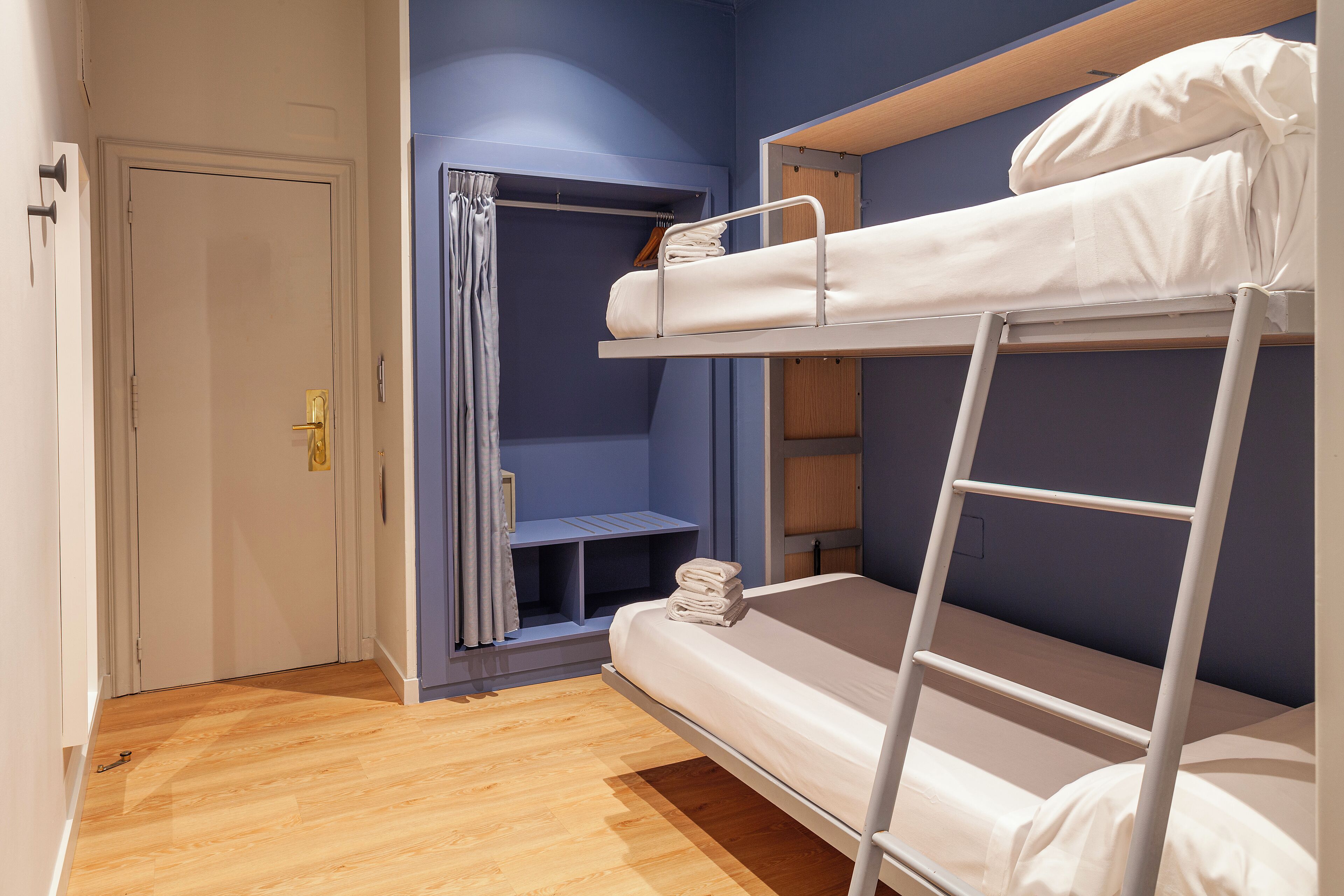 Een slaapkamer met stapelbed, houten vloer, een deur en een kledingkast.