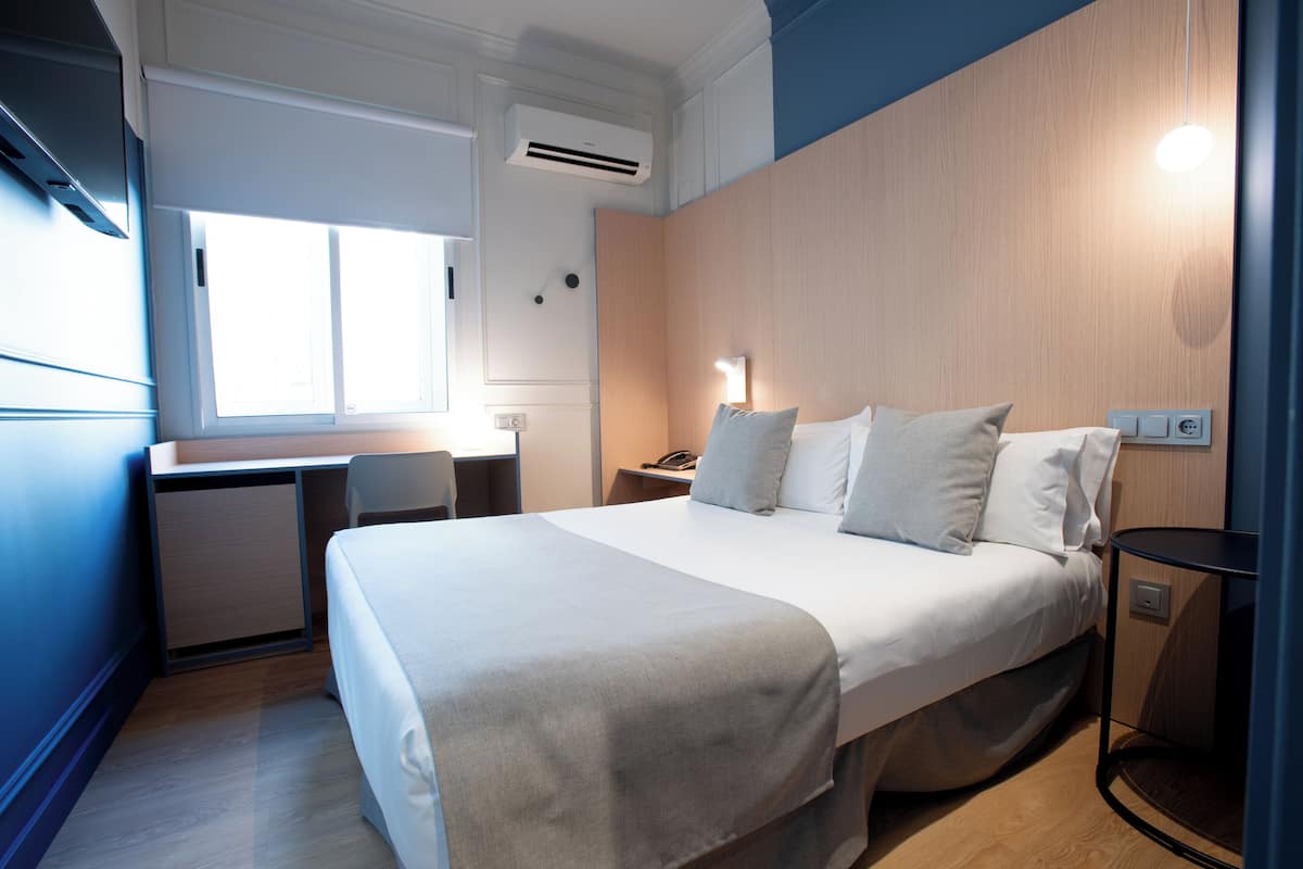 Ein Hotelzimmer mit Bett, Nachttisch, Schreibtisch und Fenster.