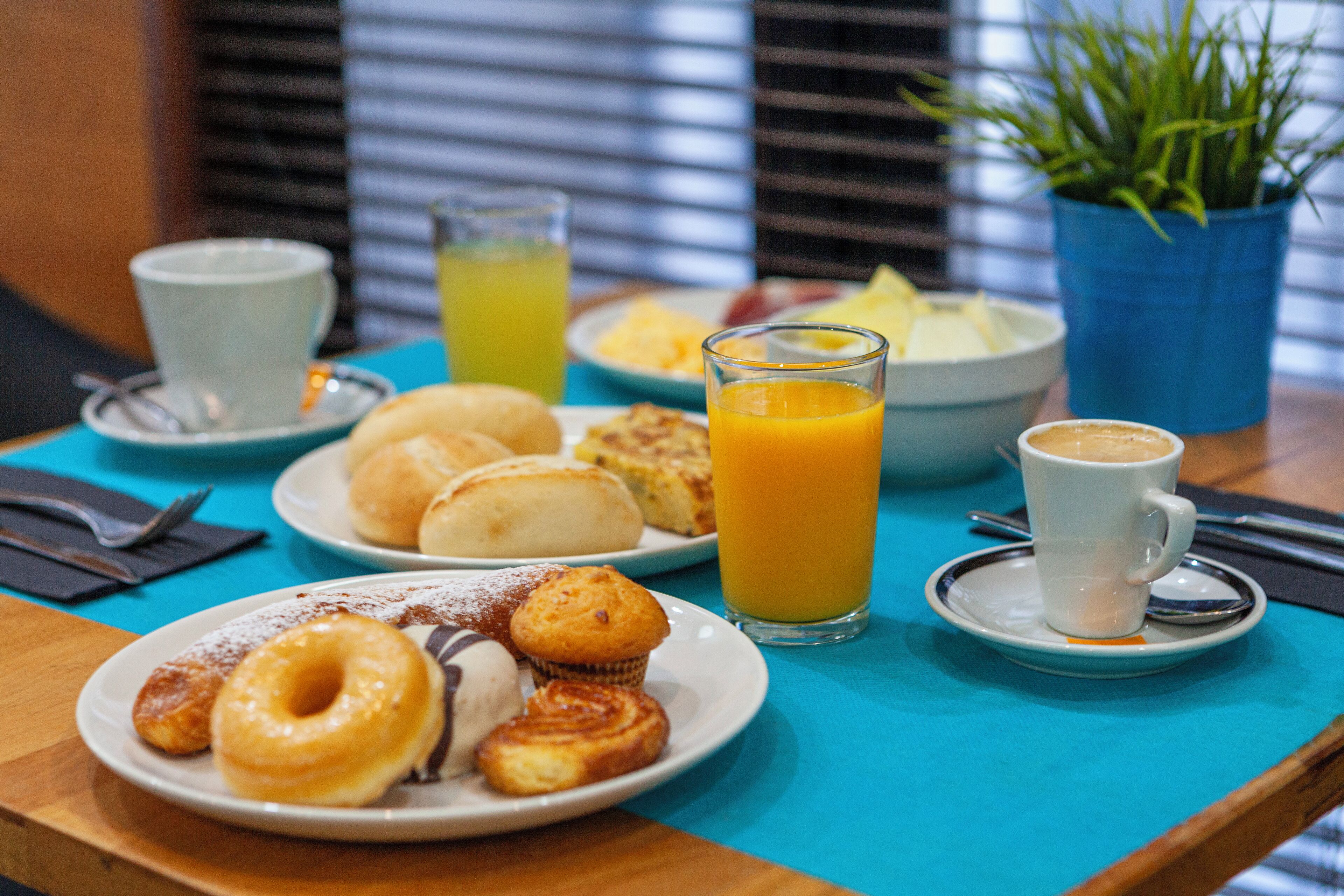 Une table de petit-déjeuner avec des assiettes de viennoiseries, un verre de jus d’orange et une tasse de café.