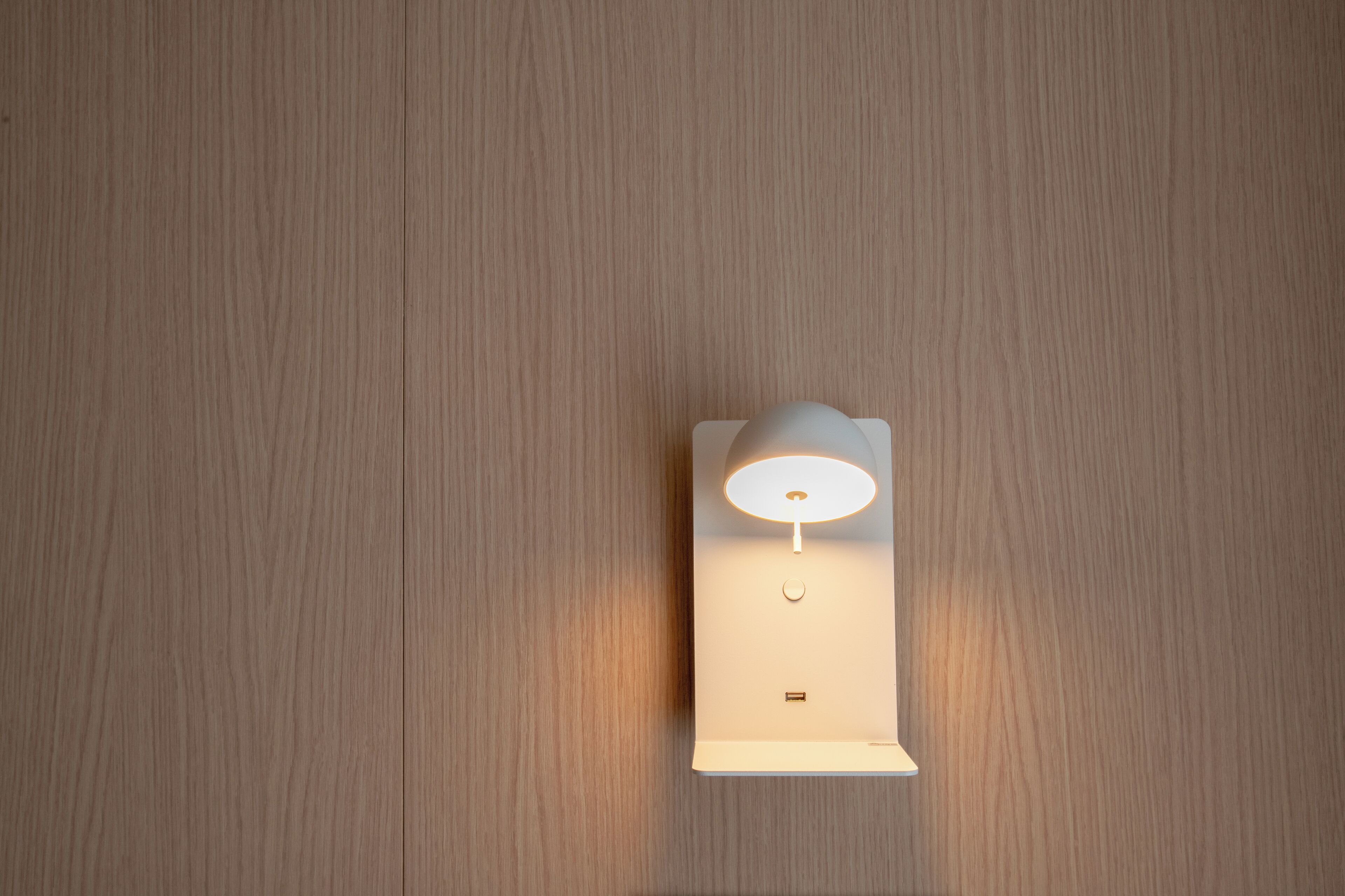 A modern wall-mounted light fixture with a white shade and a small control button below it.