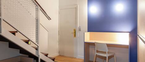 Una habitación moderna con una escalera, un escritorio y una silla, y una puerta.