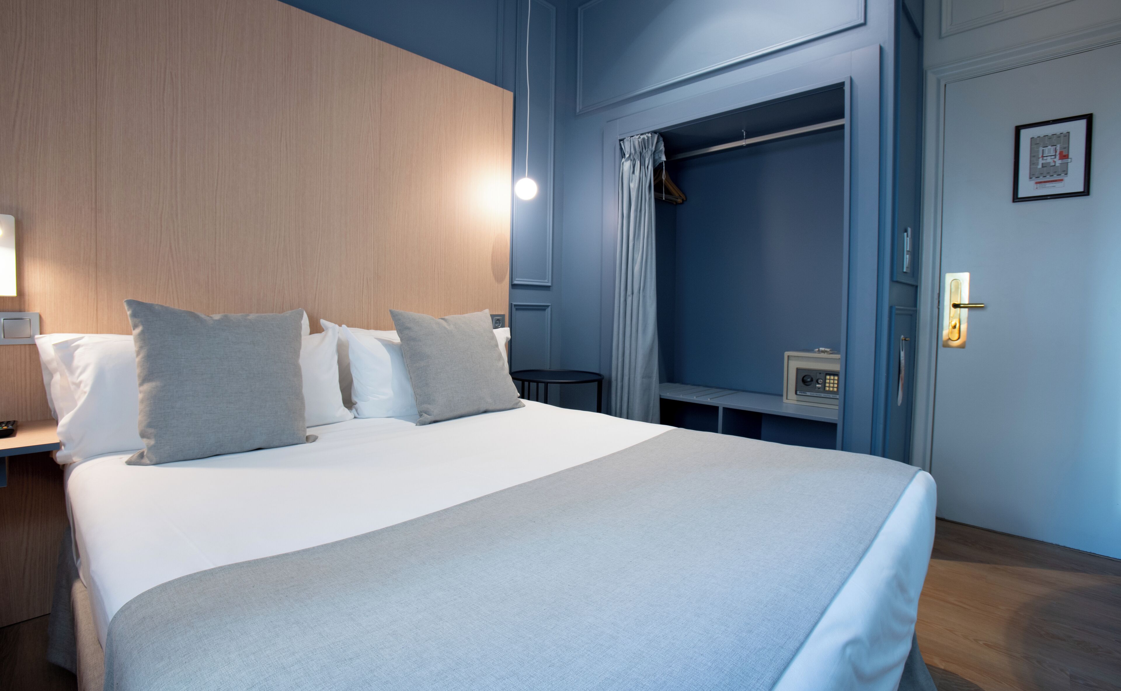 Habitación de hotel con una cama grande, una mesita de noche, un armario y una pequeña mesa con una radio.