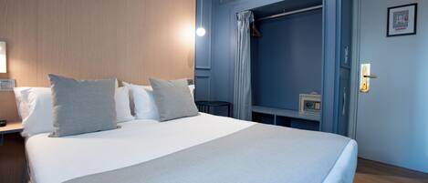 Habitación de hotel con una cama grande, una mesita de noche, un armario y una pequeña mesa con una radio.