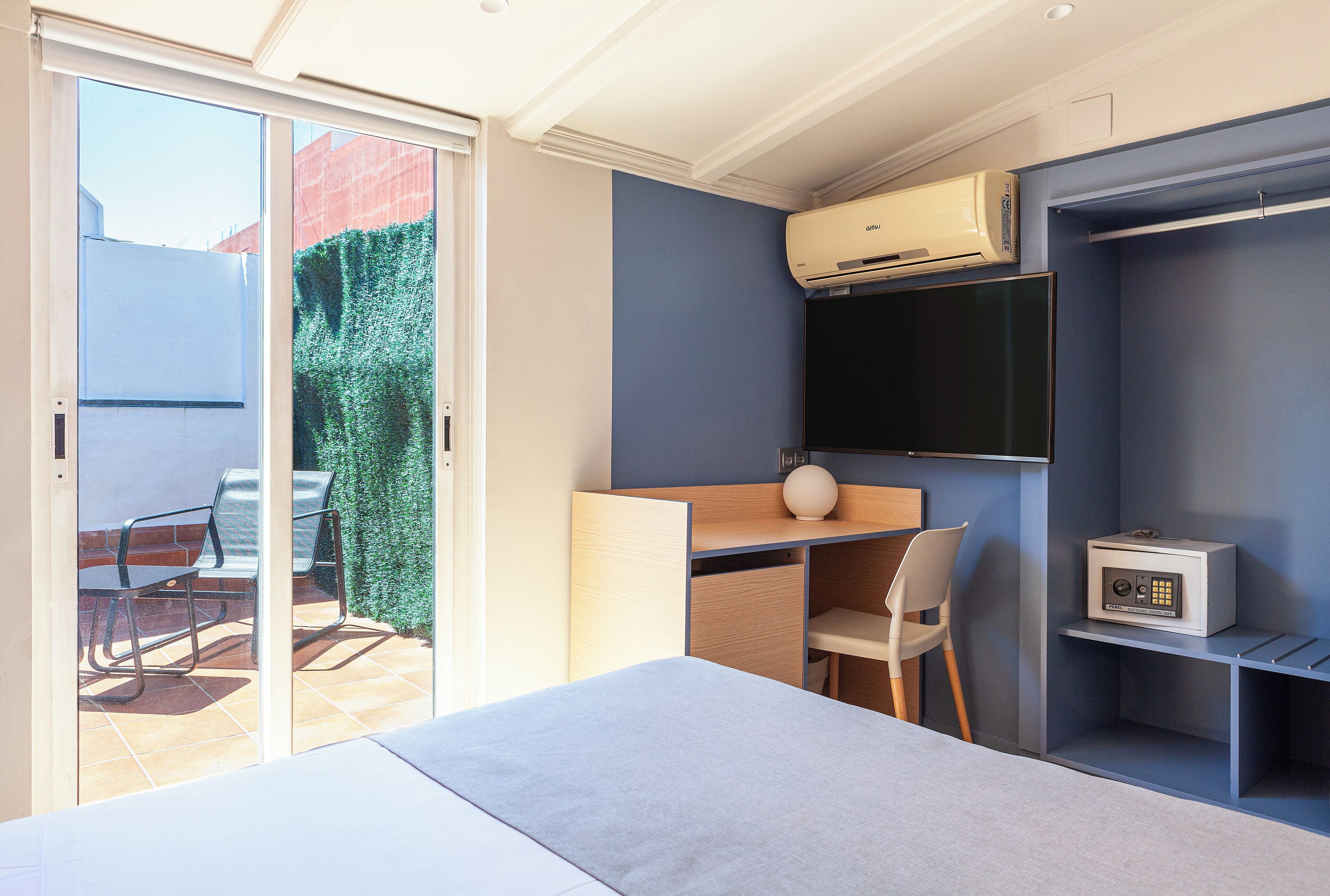 A modern room with a bed, a desk, a chair, an air conditioning unit, a television, and a safe.