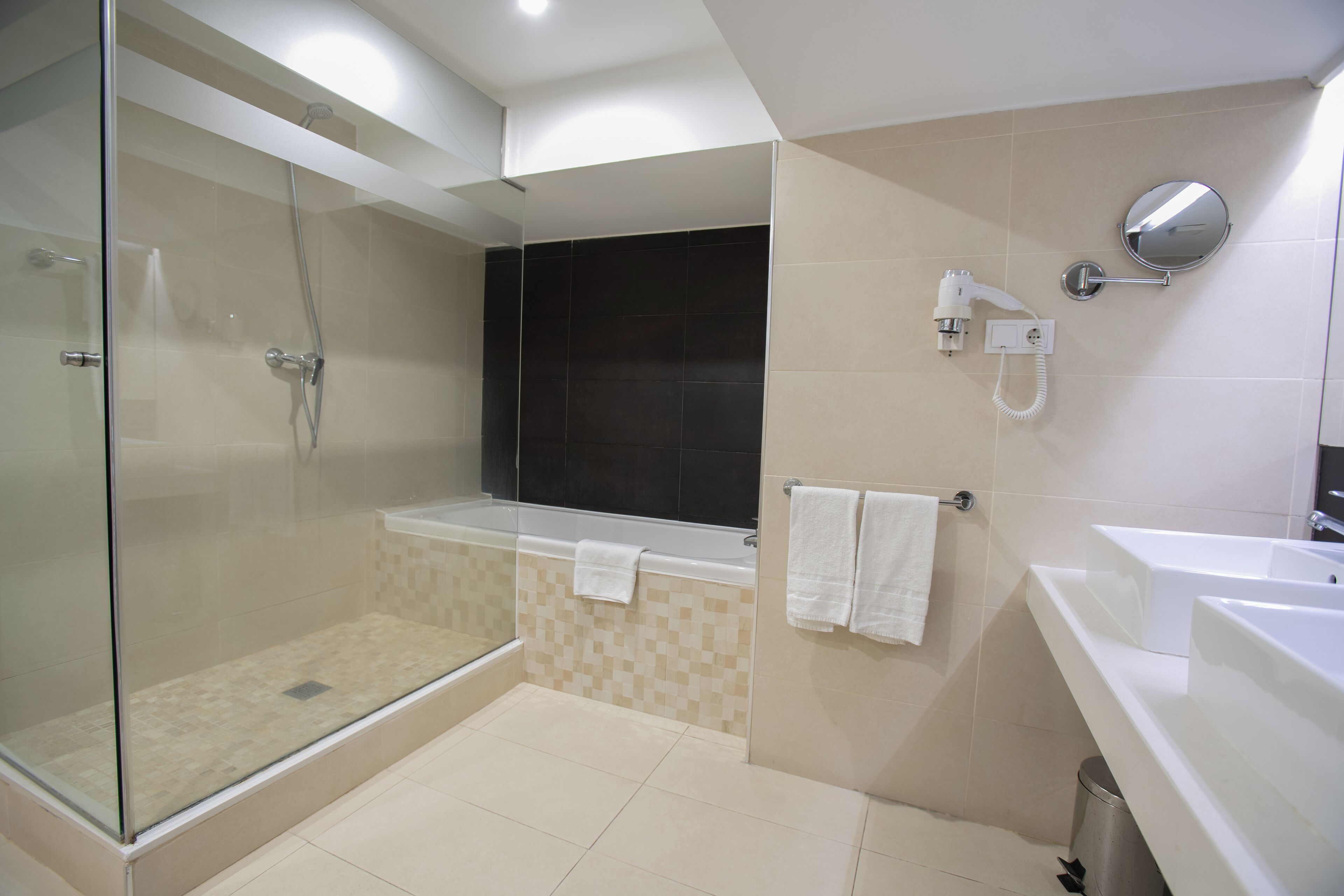 Un baño moderno con ducha envuelta en vidrio, bañera separada y tocador con espejo.