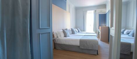 A hotel room with two beds, a wooden floor, and a blue accent wall.