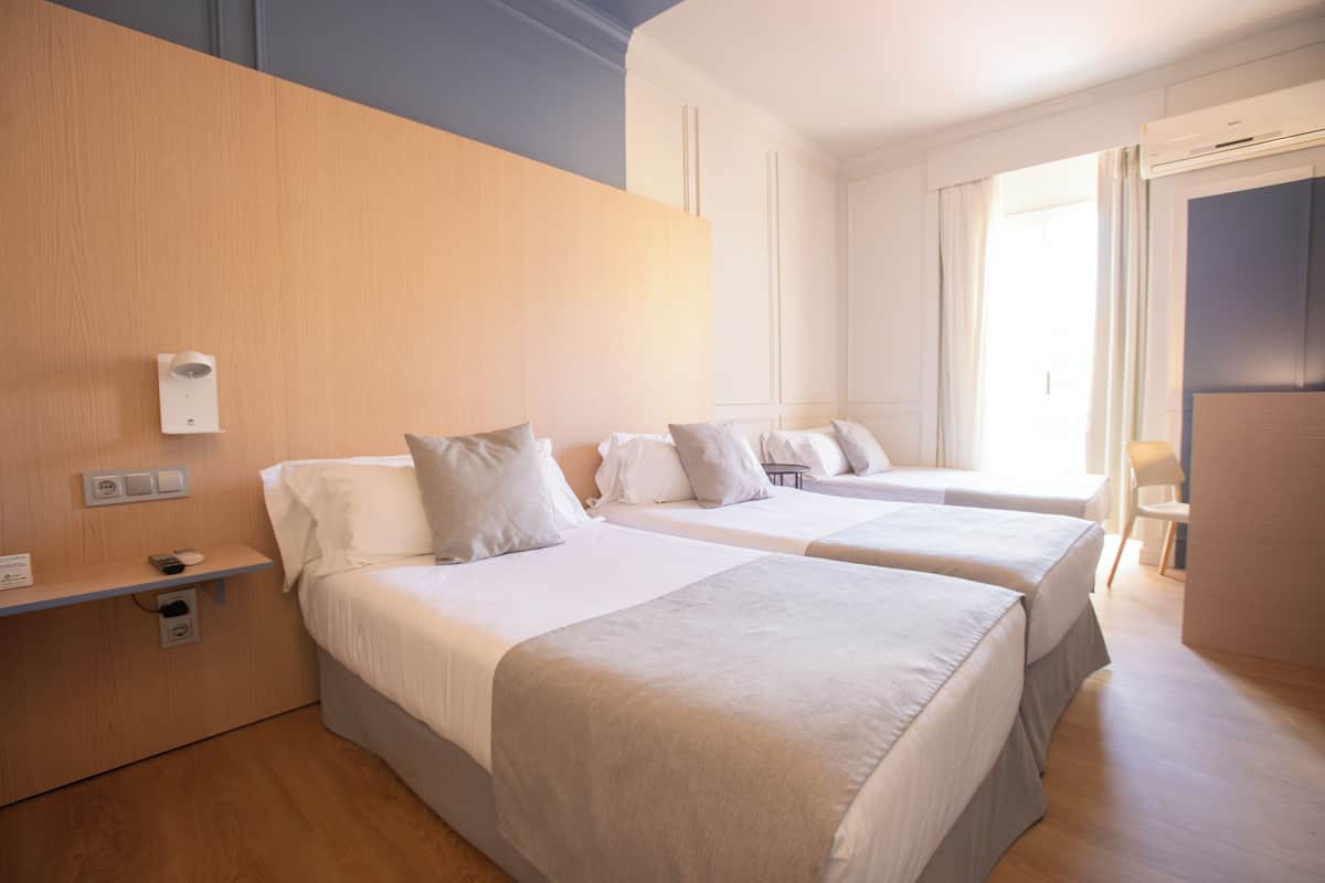 Ein Hotelzimmer mit zwei Betten, einem Holzkopfende, einem Nachttisch mit Lampe und einem Fenster mit Vorhängen.