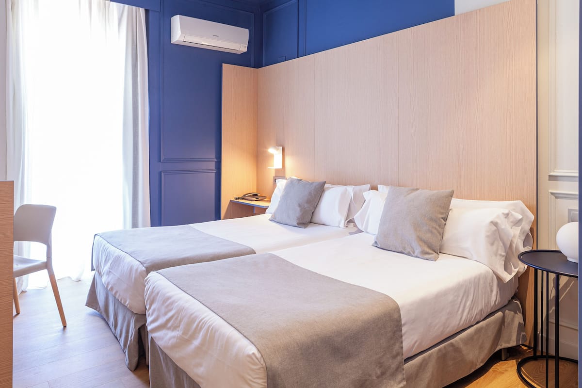 Ein Hotelzimmer mit zwei Betten, einem Nachttisch mit Lampe, einem Sessel und einem kleinen runden Tisch.