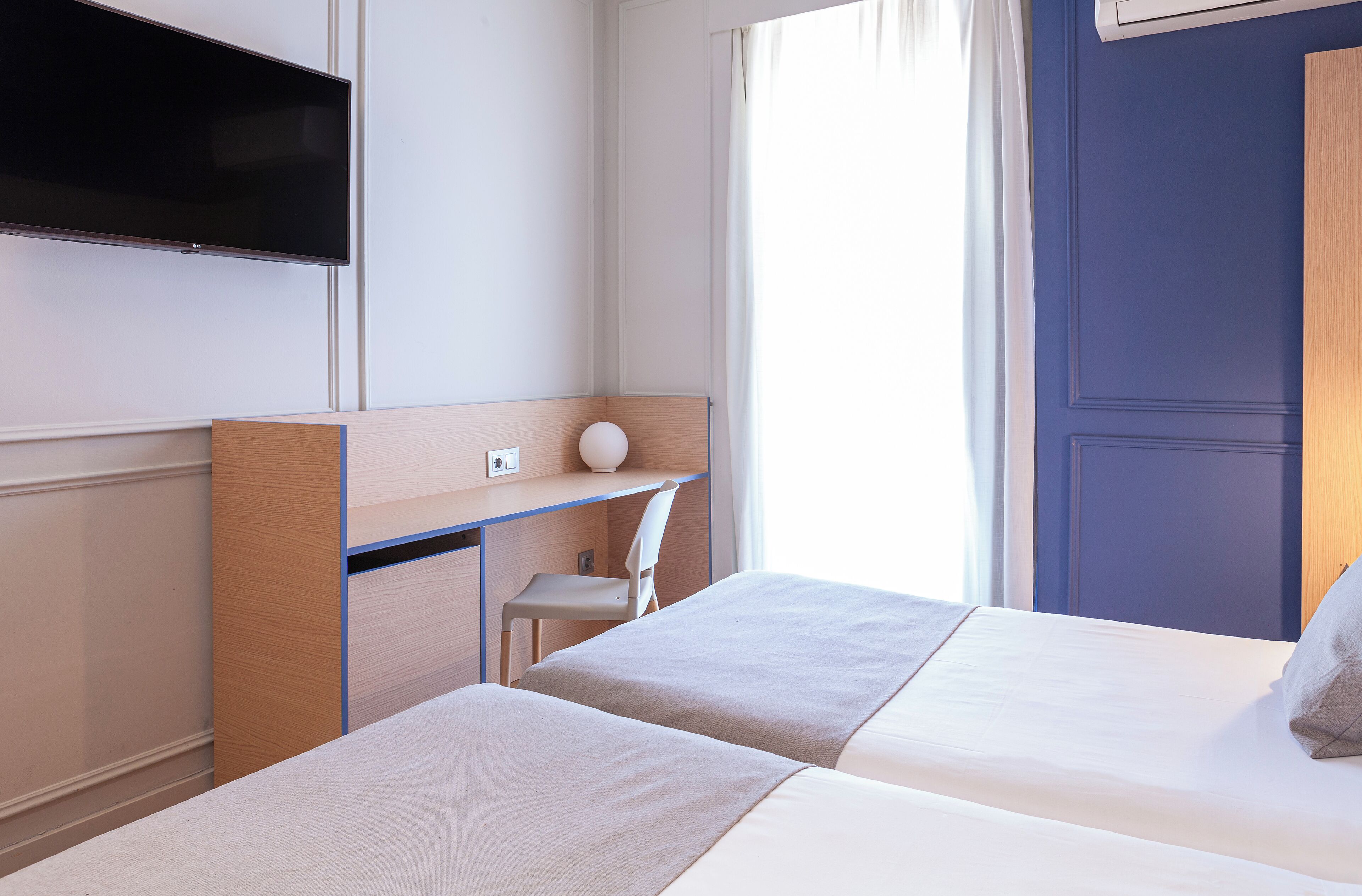 A hotel room with two beds, a desk, a chair, a TV, and a window with curtains.