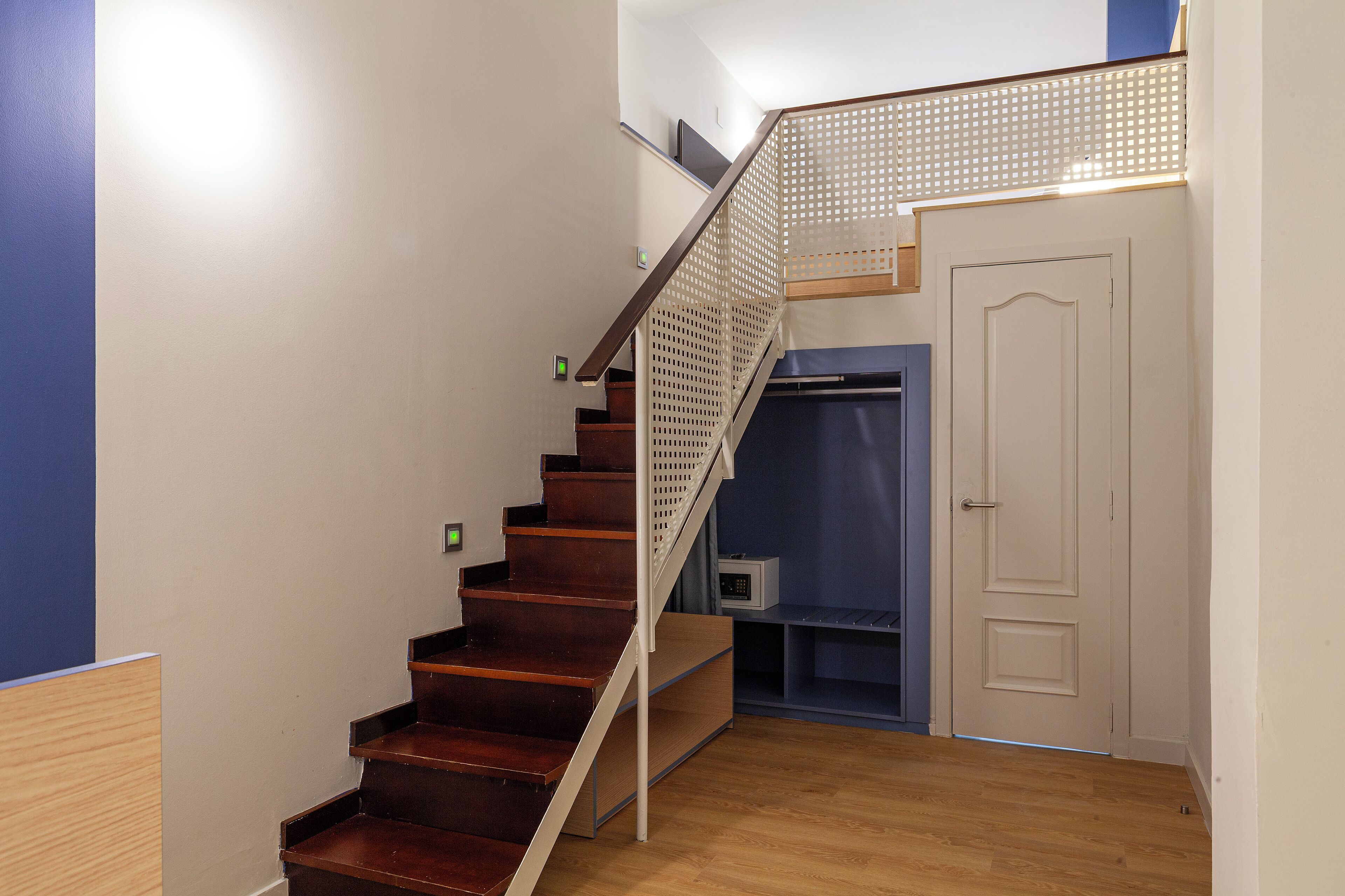 A staircase with wooden steps and a metal handrail, leading to a door with a small shelf below.