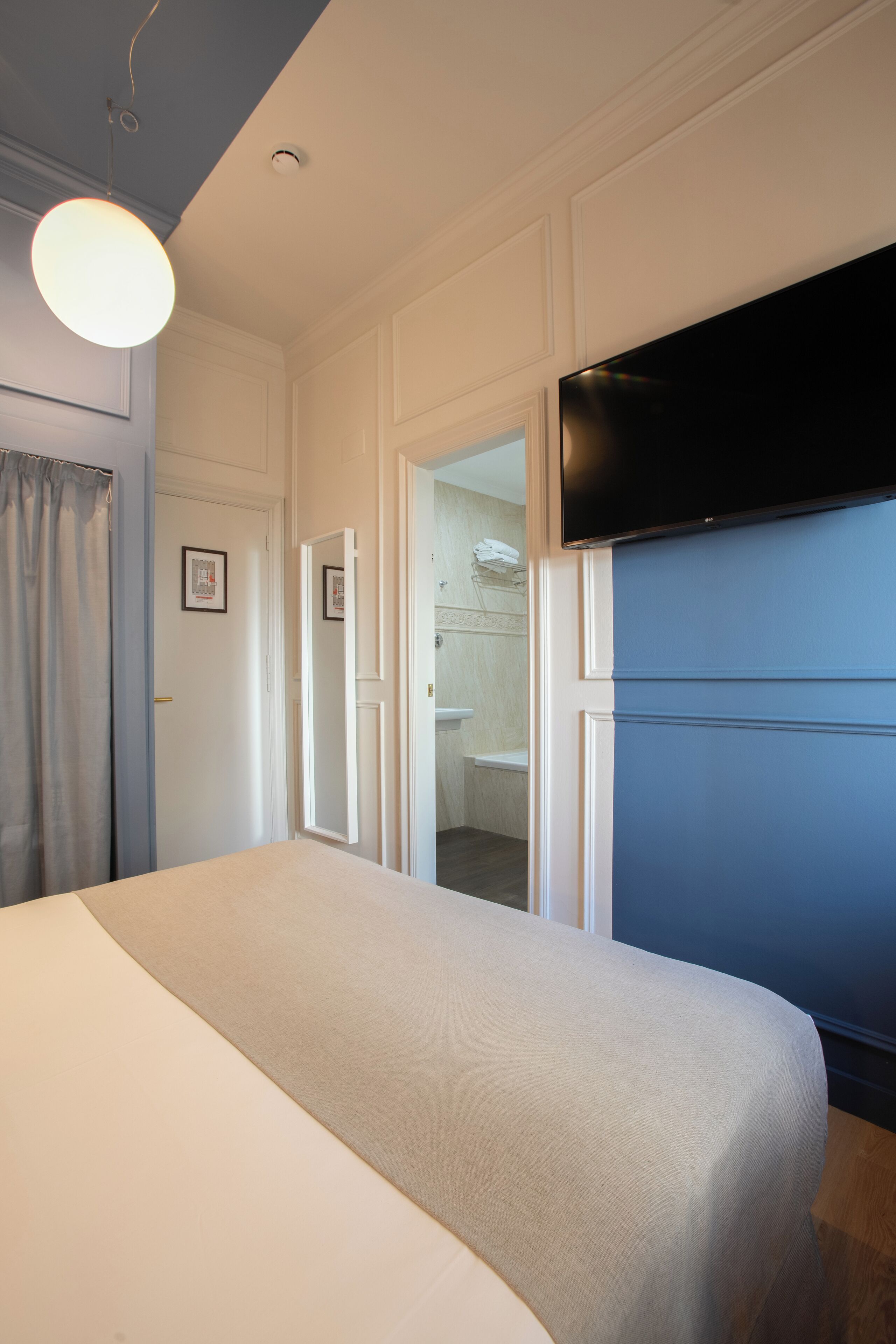 Une chambre comprenant un lit, un téléviseur à écran plat fixé au mur, une porte donnant accès à une salle de bain et un luminaire placé au-dessus du lit.