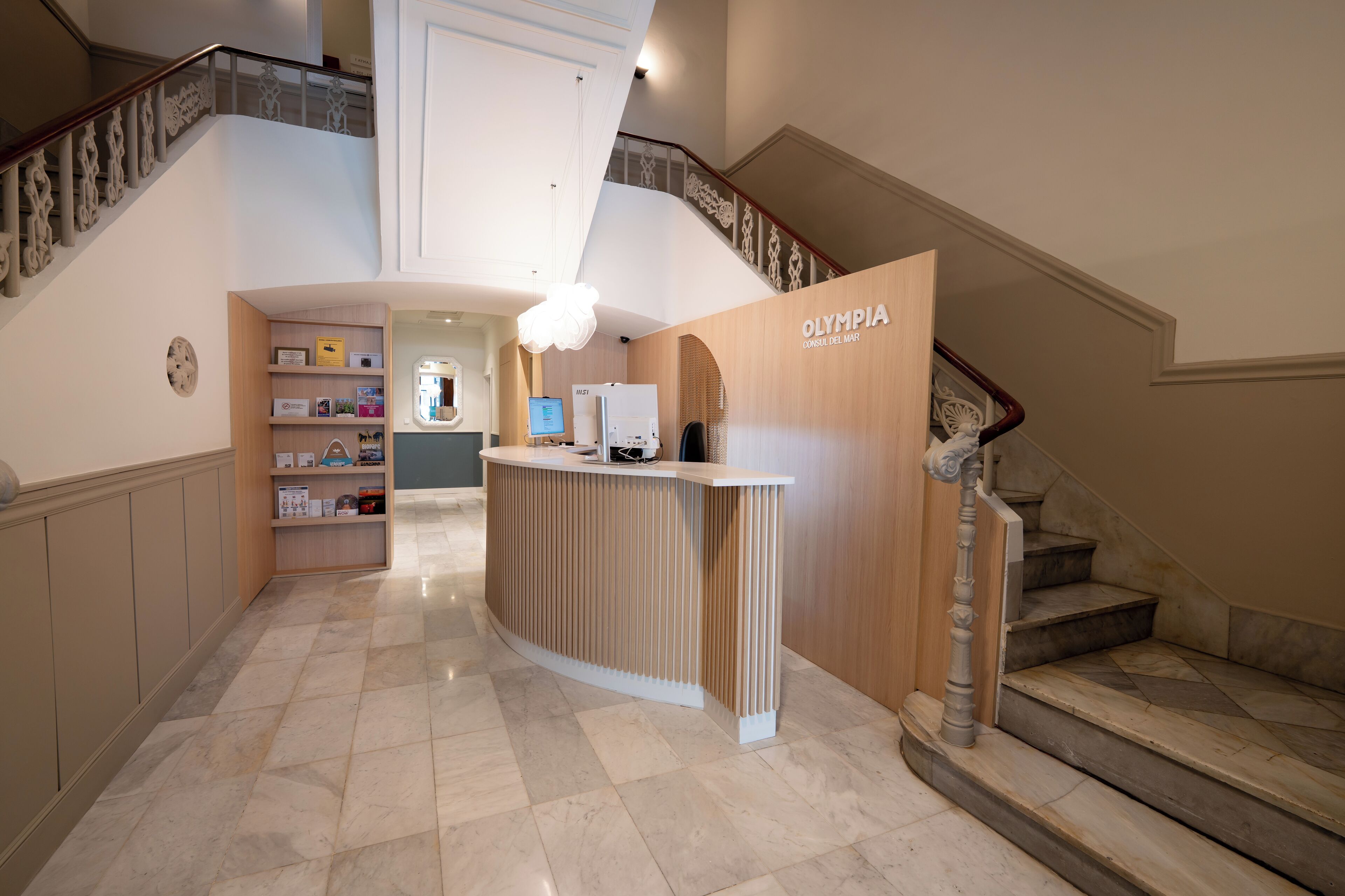Zona de recepción con mostrador de madera, una escalera y un pasillo que conduce a una habitación con escritorio y computadora.