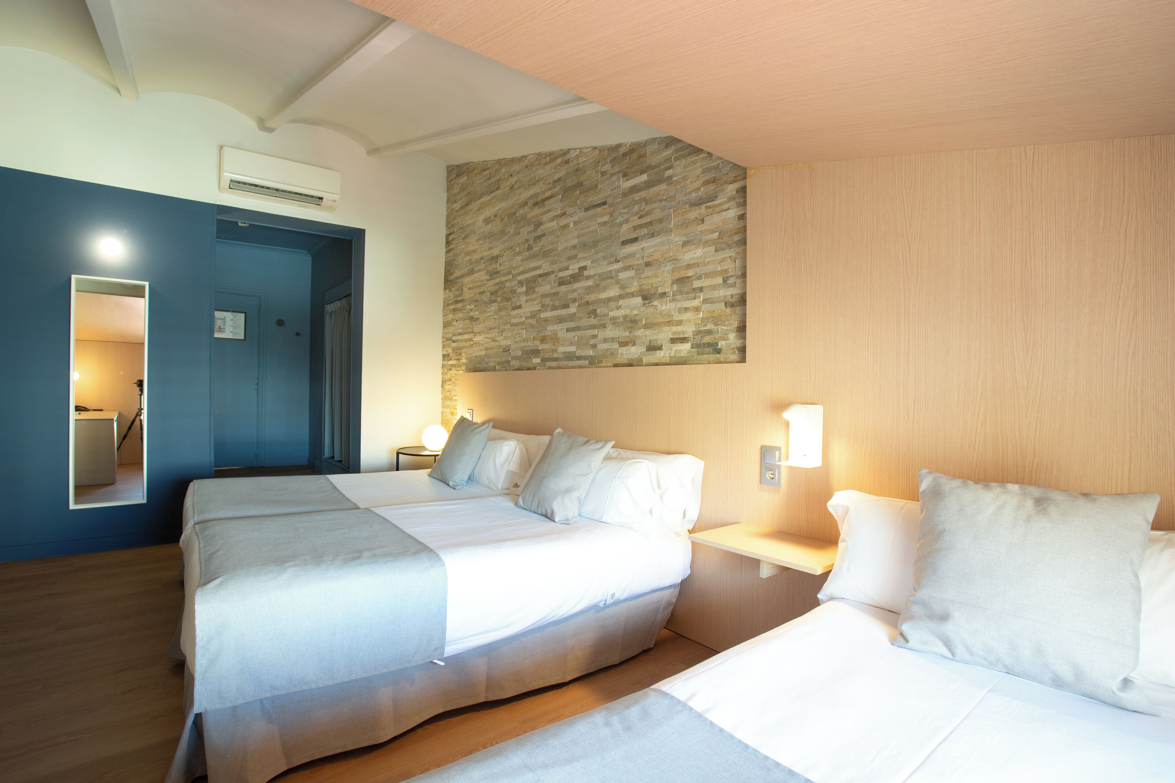 Een hotelkamer met twee bedden, een accentmuur van steen en een houten plafond.