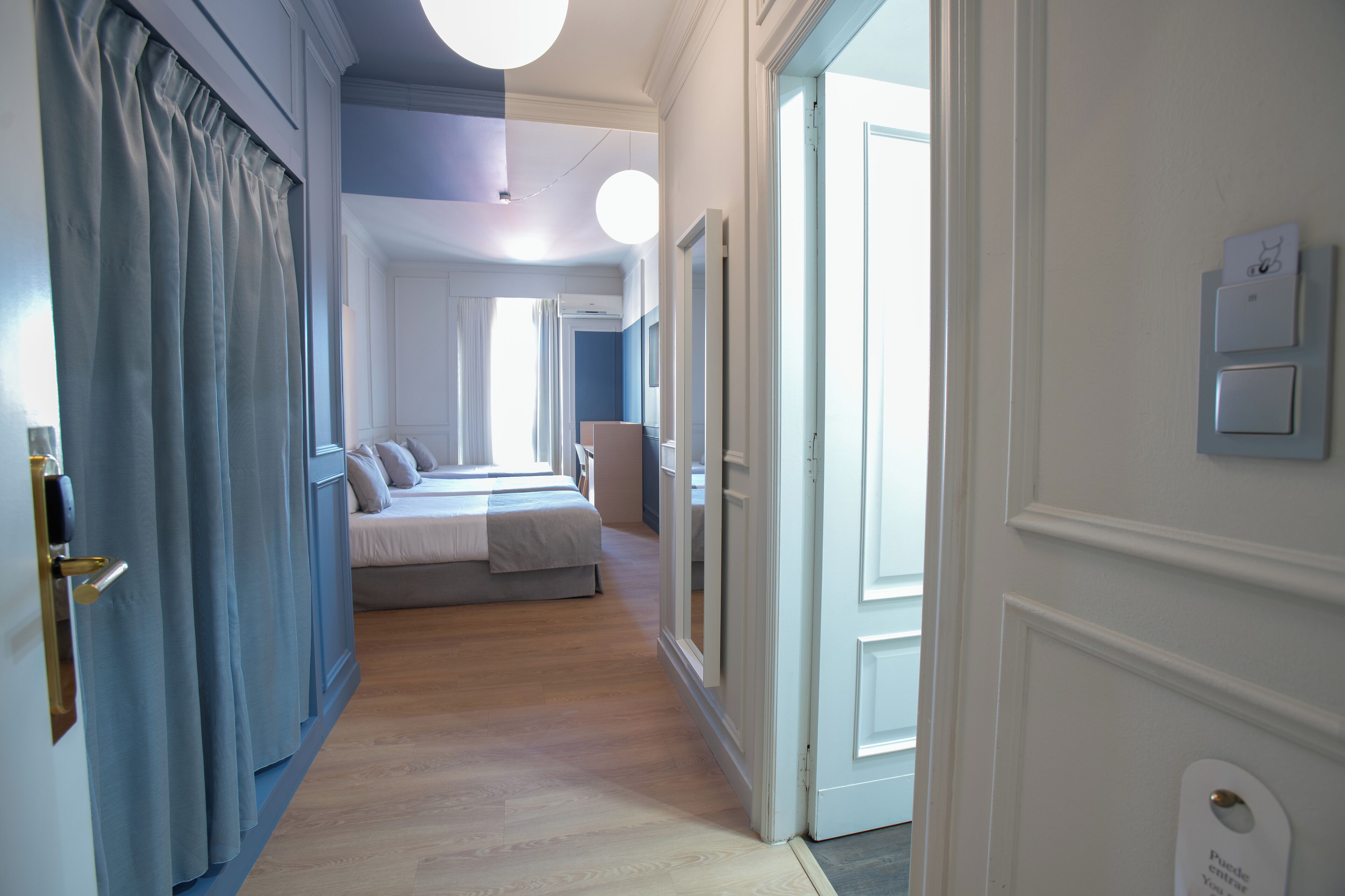 Een hotelgang met een bed, een deur en een lichtschakelaar aan de muur.