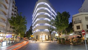 Un hotel moderno con fachada curva, varios balcones y una entrada bien iluminada.