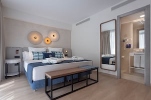 Moderni hotellihuone, jossa on sänky, yöpöydät, penkki, suuri peili ja kylpyhuone, joka näkyy avoimesta ovesta.