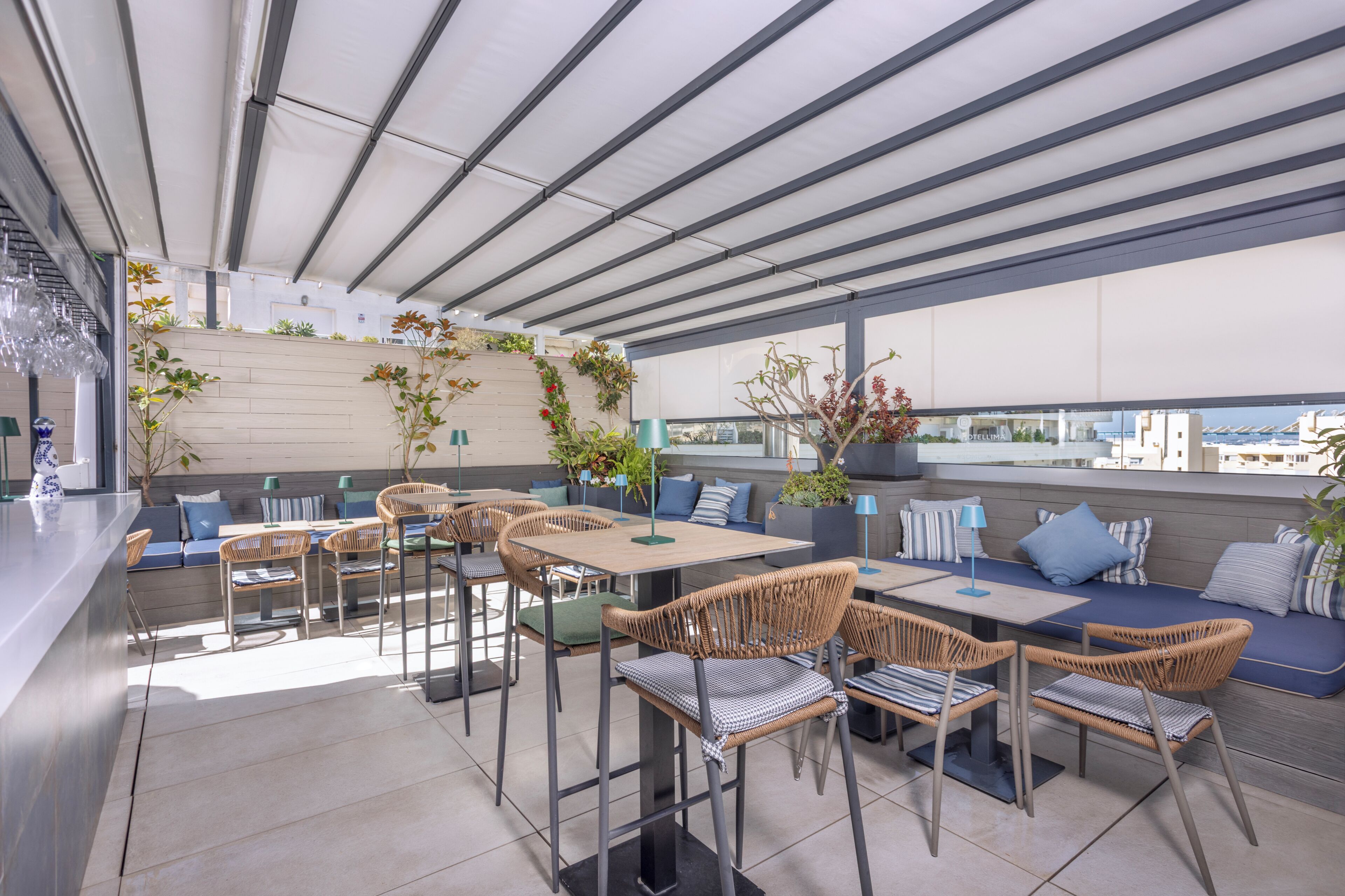 En udendørs terrasse med siddepladser, borde og stole, med udsigt over byen.