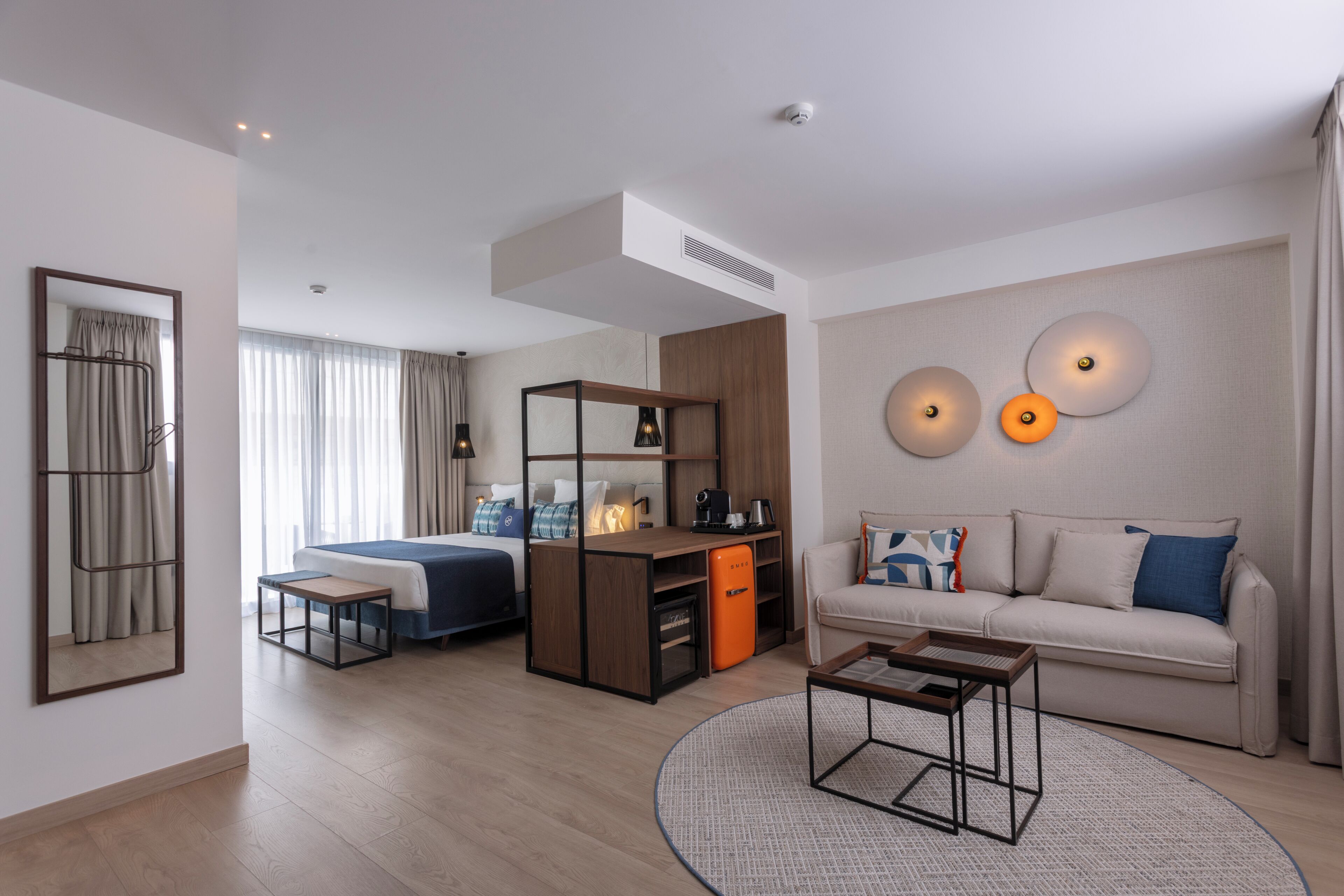 A modern hotel room with a bed, desk, sofa, and a round coffee table.