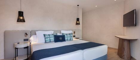 A modern hotel room with a large bed, two bedside tables, a TV, and pendant lighting.
