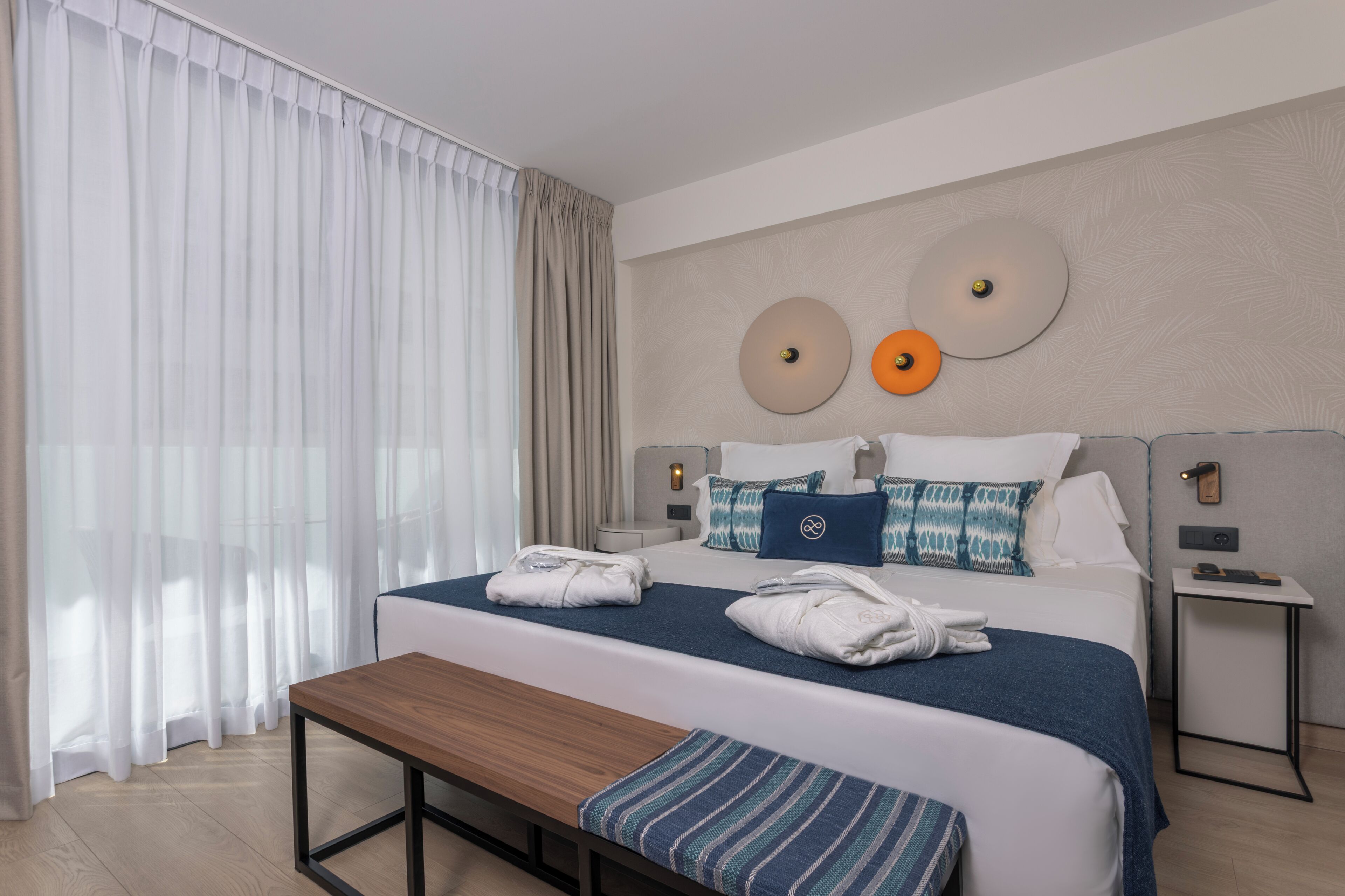 Ein Hotelzimmer mit einem großen Bett, Nachttischen, einer Bank und Blick ins Freie.