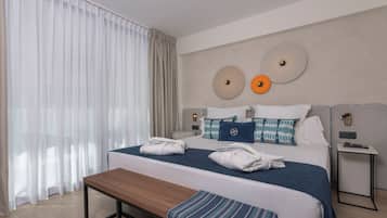 A hotel room with a large bed, bedside tables, a bench, and a view of the outdoors.