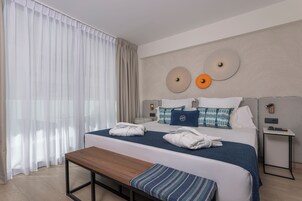 Een hotelkamer met een groot bed, nachtkastjes, een bankje en uitzicht op het omliggende landschap.