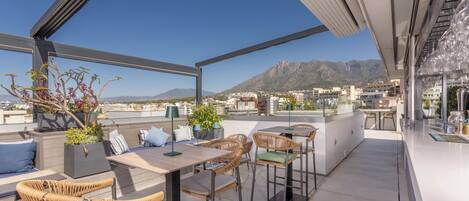 Une terrasse sur le toit, aménagée avec du mobilier d’extérieur, un espace repas et offrant une vue sur la ville et les montagnes.
