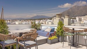 Terraza en la azotea con mobiliario exterior, un sofá y vistas a la ciudad y montañas.