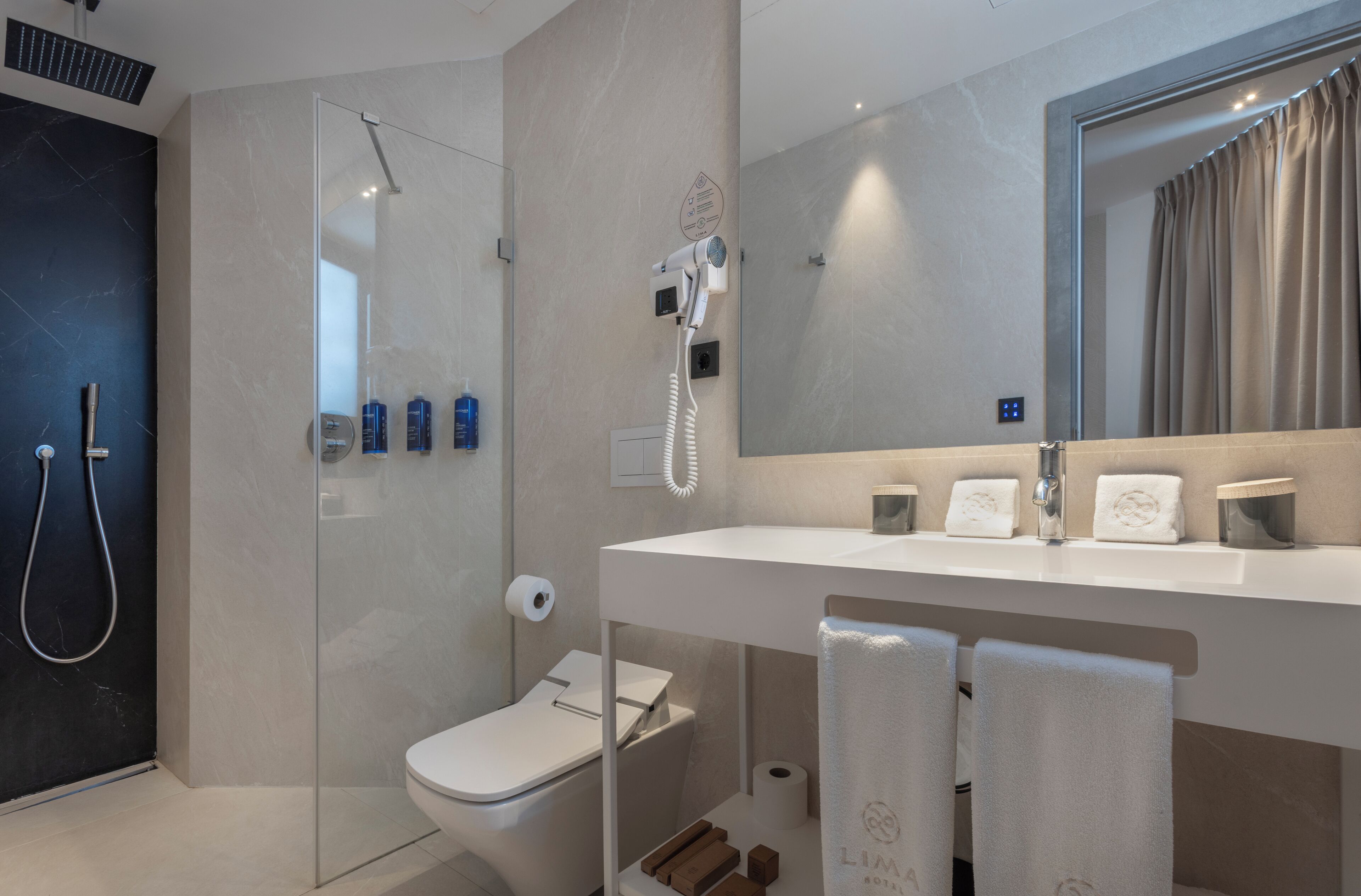 Een moderne badkamer met een douchecabine van glas, toilet, wastafel met spiegel en een handdoekhouder.
