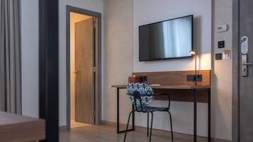 Ett modernt hotellrum med ett skrivbord i trä, en stol, en platt-TV som är monterad på väggen och en dörr som leder till ett annat rum.