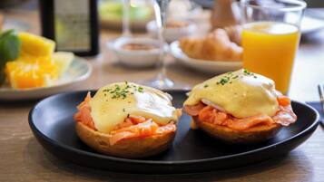 A breakfast setting with eggs benedict sandwiches, a glass of orange juice, and a plate of fruit.