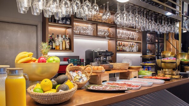 Un bufé de desayuno con diversas opciones de comida, una máquina de café y una zona de bar con botellas y vasos.