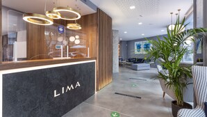 Un área de recepción moderna con un letrero 'LIMA', paneles de madera y una zona de estar con sillas estampadas y una planta en maceta.