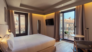 Habitación de hotel con cama, televisión, balcón y vista a edificios, además de una pequeña mesa.