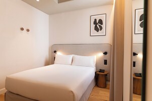 Moderni hotellihuone, jossa on suuri sänky, yöpöydät ja peili.
