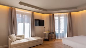 Una habitación de hotel moderna con un sofá, una pequeña mesa con una silla, una cama y un televisor montado en la pared.