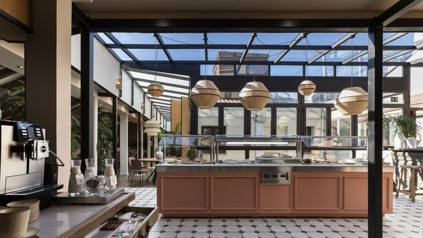 Un café moderno con una isla central, máquinas de café y un área de comedor con paredes de vidrio.