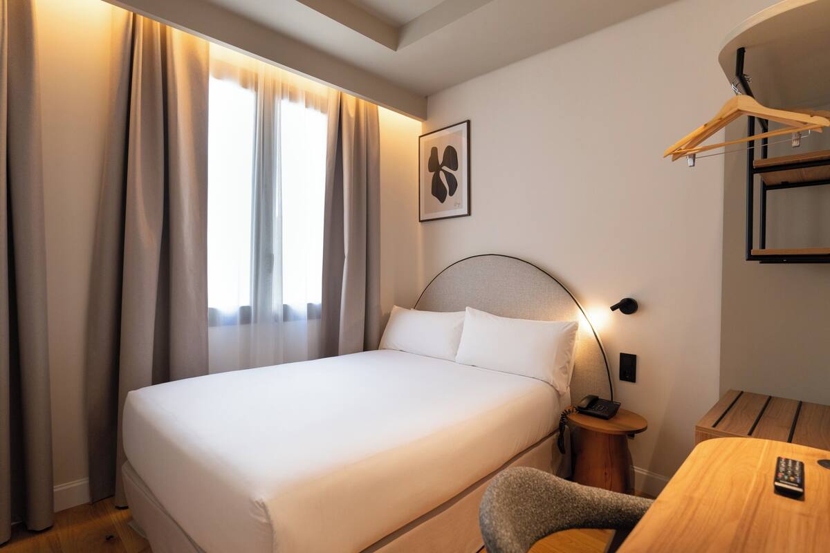 A neatly made bed with white linens, a bedside table with a lamp, and a wooden chair.