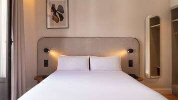 Habitación de hotel con una cama grande, mesitas de noche, un reloj de pared, una obra de arte enmarco y un espejo.