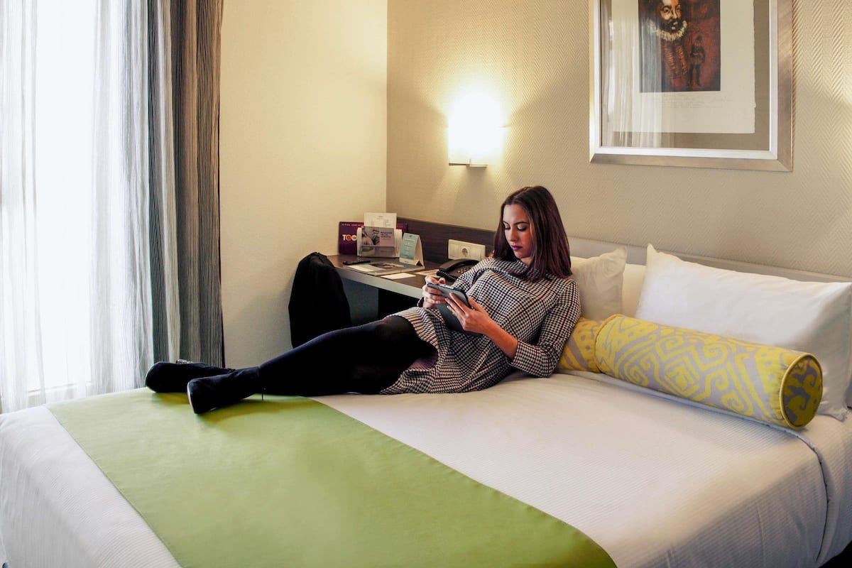 A hotel room with a bed, a desk, and a lamp.