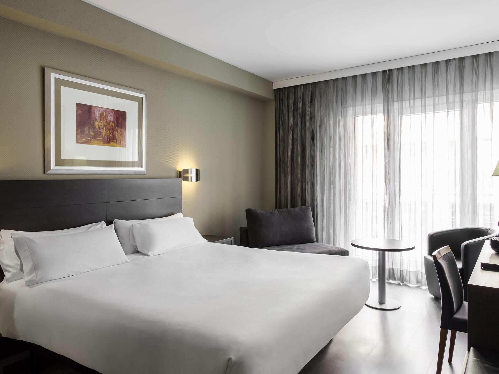 Habitación de hotel con una cama grande, un escritorio, una silla, una mesita y un cuadro en la pared.