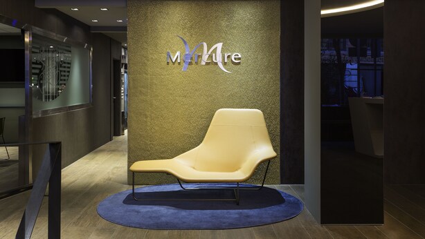 A modern interior with a reception desk, a lounge chair, and a textured wall with the 'Mature' logo. - Mercure Madrid Centro (Madrid)