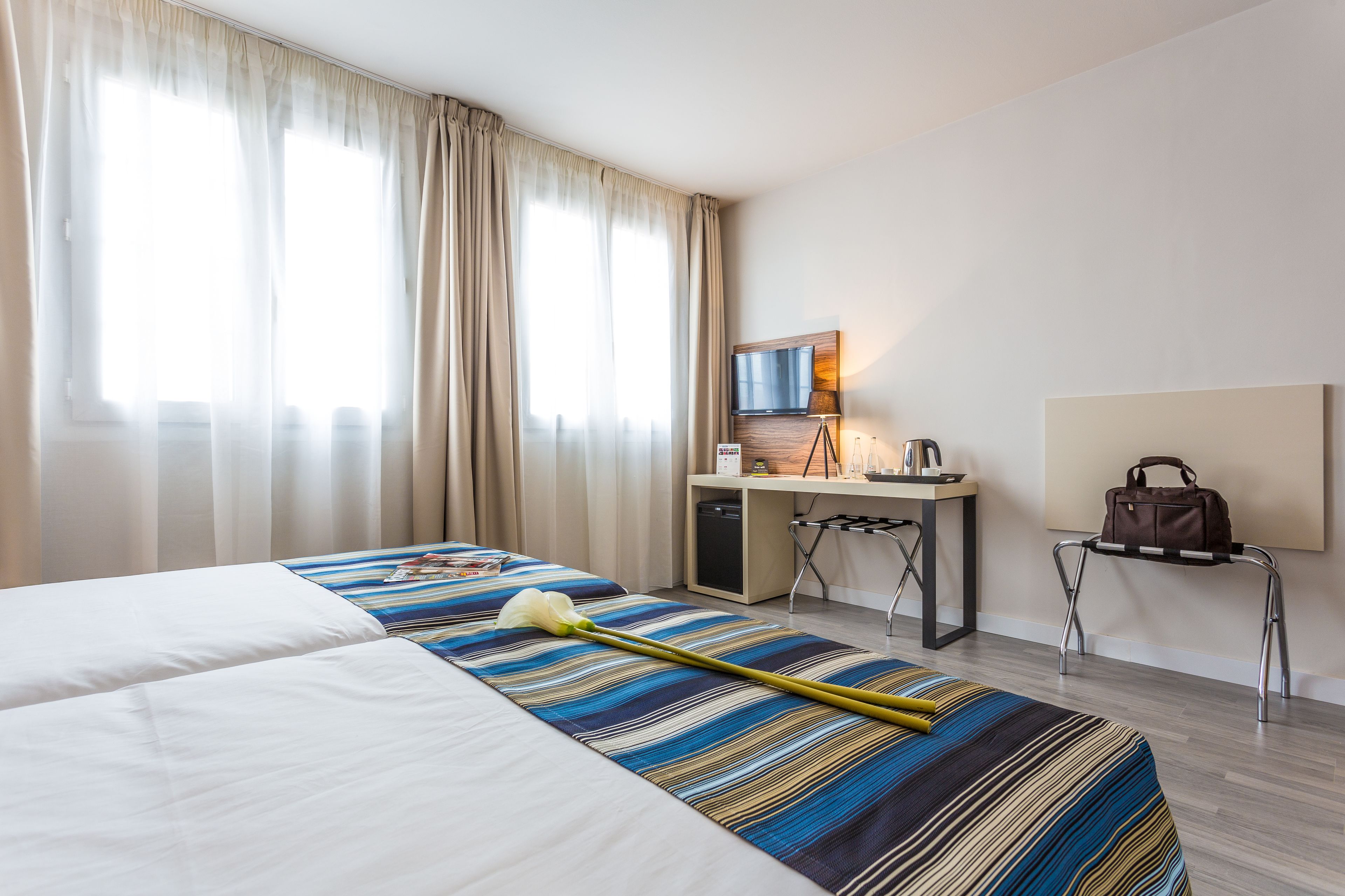 Habitación de hotel con dos camas, un escritorio, una silla, un televisor y un bolso sobre un atril.