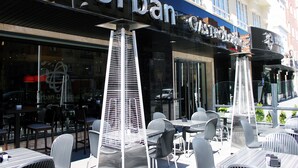 Un espace extérieur aménagé avec des tables et des chaises, un bâtiment sur lequel on peut lire l’inscription « Urban Design », et une vue dégagée sur la rue en arrière-plan.