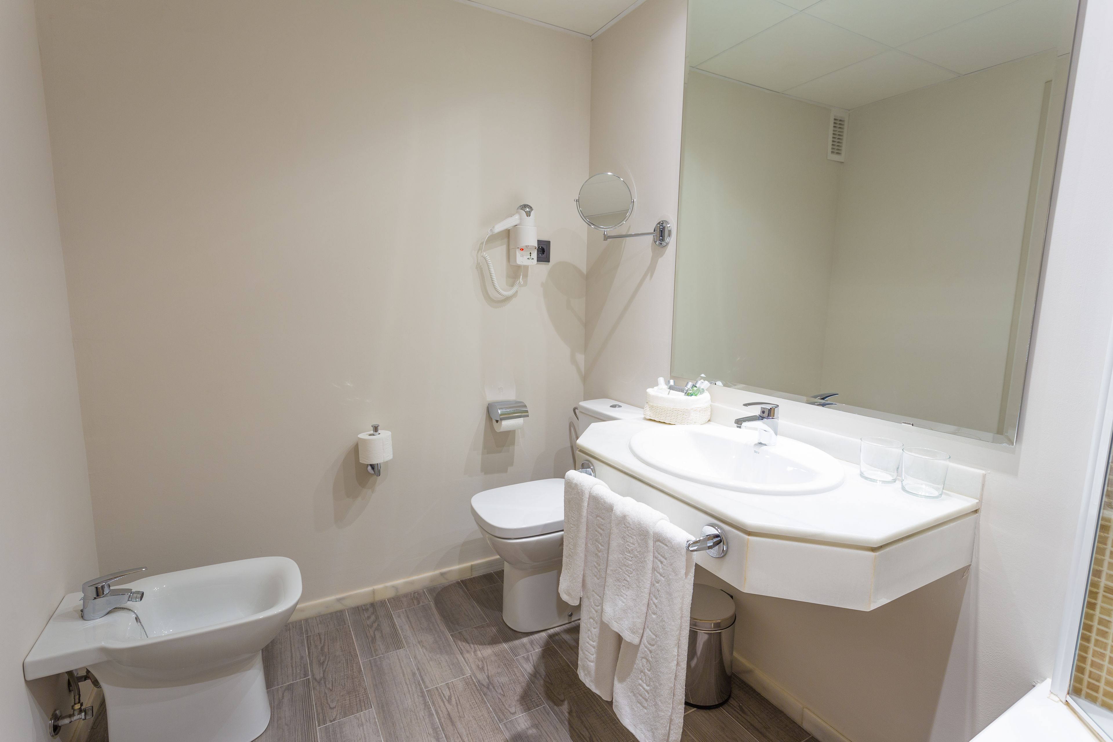 Et badeværelse med bidét, toilet, håndvask og spejl.