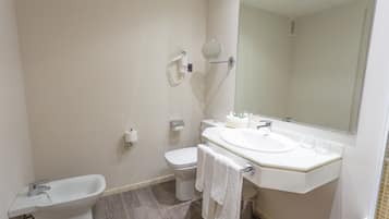 Et badeværelse med bidét, toilet, håndvask og spejl.