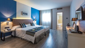 Une chambre d’hôtel moderne, dotée d’un grand lit, de tables de chevet, d’un bureau et d’une salle de bain visible à travers une porte ouverte.