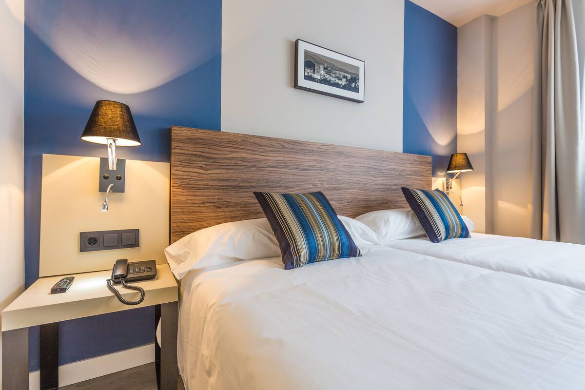 A hotel room with a large bed, two bedside lamps, a nightstand with a phone, and a framed picture on the wall.