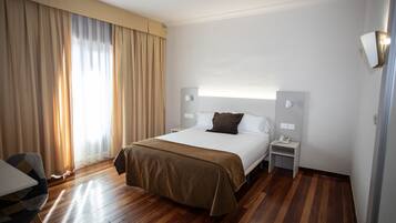 A hotel room with a bed, bedside tables, a chair, and a large window with curtains.