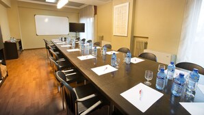Un salón de conferencias con una larga mesa, sillas, botellas de agua y una pizarra.